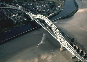 The Mersey Bore passing the Runcorn road and railway bridges, following the main channel (right to left) just before reaching the wall of the Manchester Ship Canal where it gets reflected